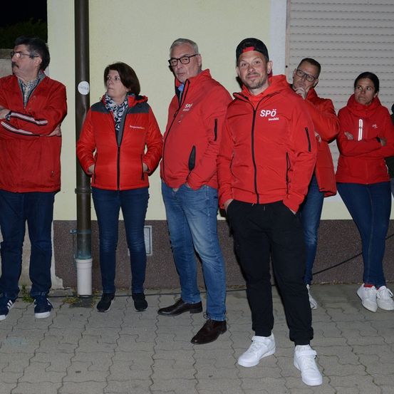 Eine Gruppe von Menschen in roten Jacken steht vor einem Gebäude, möglicherweise für ein Foto.