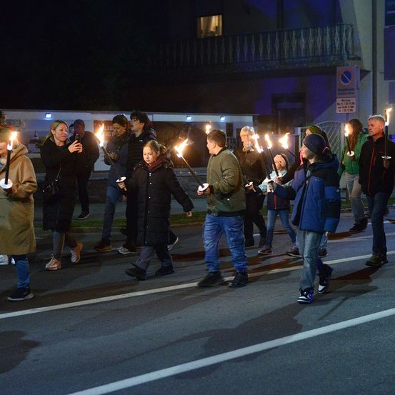Eine Gruppe von Menschen geht nachts auf der Straße und hält brennende Kerzen in den Händen. Sie sind in Winterkleidung gekleidet.