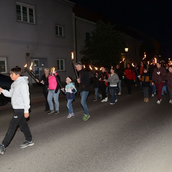 Eine Gruppe von Menschen geht nachts mit brennenden Fackeln in der Hand die Straße entlang. Sie sind in Winterkleidung gekleidet.