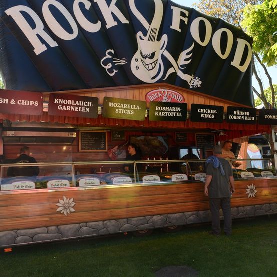 Ein Food-Truck mit Rock-Thema, der verschiedene Gerichte wie Fisch und Pommes, Mozzarella-Sticks und Hähnchenflügel anbietet. Ein Mann steht vor dem Tresen.