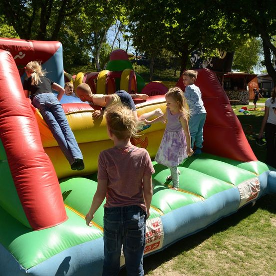 Eine Gruppe von Kindern spielt auf einem großen aufblasbaren Rutschen in einem Park, mit einigen Erwachsenen in der Nähe.