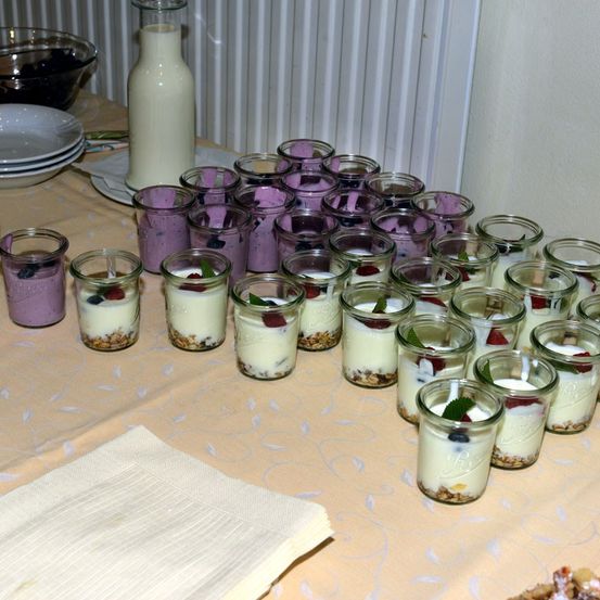 Ein Tisch mit mehreren Gläsern mit Joghurt, überzogen mit Beeren und Müsli, einer Schüssel mit Beeren und einer Milchflasche.