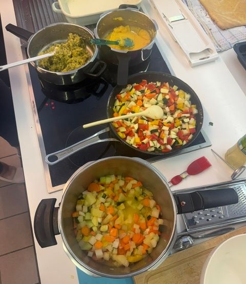 Eine Küchentheke mit drei Töpfen mit gemischtem Gemüse auf einem Herd, einer Schüssel mit gemischtem Gemüse und einer Käsereibe auf der Theke.