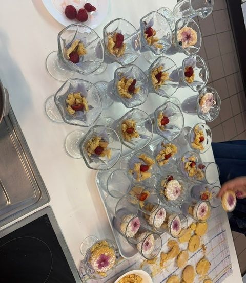Ein Tisch mit mehreren Gläsern, die mit einem Dessert gefüllt sind, das mit Erdbeeren und einer Blume auf der Oberseite verziert ist.