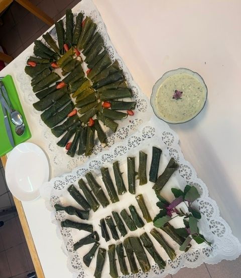 Zwei Teller mit grünen Gemüserollen sind auf einem Tisch angeordnet. Ein Teller hat eine kreisförmige Anordnung mit roten Akzenten, während der andere ein Spiraldesign hat. Ein Schälchen mit grüner Dipsauce steht rechts.