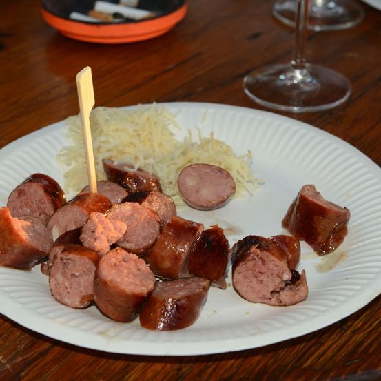 Ein weißer Teller mit mehreren gegrillten Würstchen und einer kleinen Portion Käse auf der Seite. Ein Holzspieße steckt in einem der Würstchen.