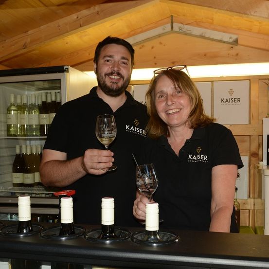 Ein Mann und eine Frau in schwarzen Kaiser-Shirts lächeln und halten Weinglas in einem Weinladen.