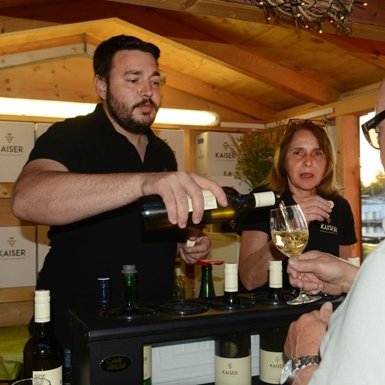 Ein Mann füllt Wein in ein Glas, das von einer Frau bei einer Weinverkostung gehalten wird.