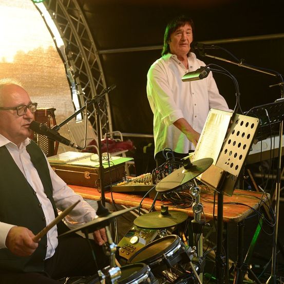 Zwei Männer spielen auf der Bühne mit Musikinstrumenten. Einer spielt die Drums, der andere das Klavier.