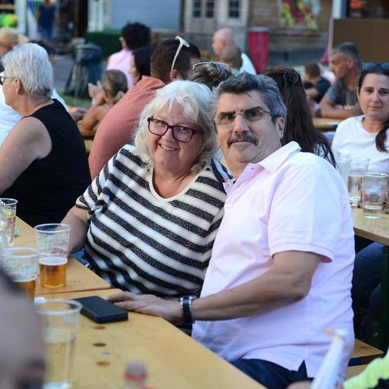 Ein Paar in einem Biergarten, lächelnd an einem Tisch mit Biergläsern sitzend.