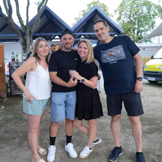 Vier Menschen stehen in einem Außenbereich und lächeln für ein Foto. Zwei Männer und zwei Frauen, wobei einer der Männer ein Hard Rock Cafe T-Shirt trägt.