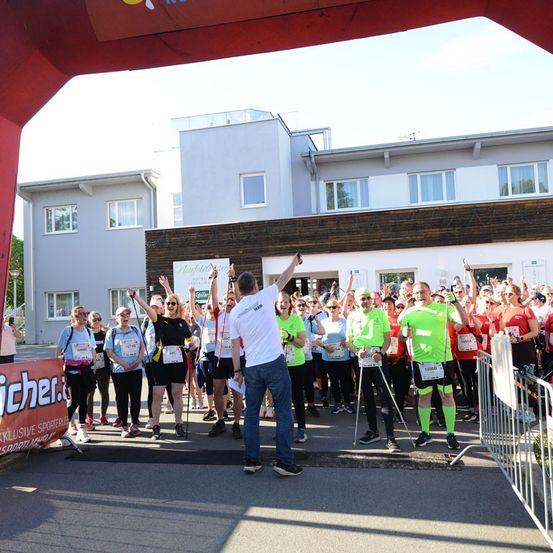 Eine Gruppe von Läufern in grünen Shirts und schwarzen Hosen versammelt sich am Start eines Marathons, mit einem Mann in einem weißen Shirt und blauen Jeans vor ihnen.