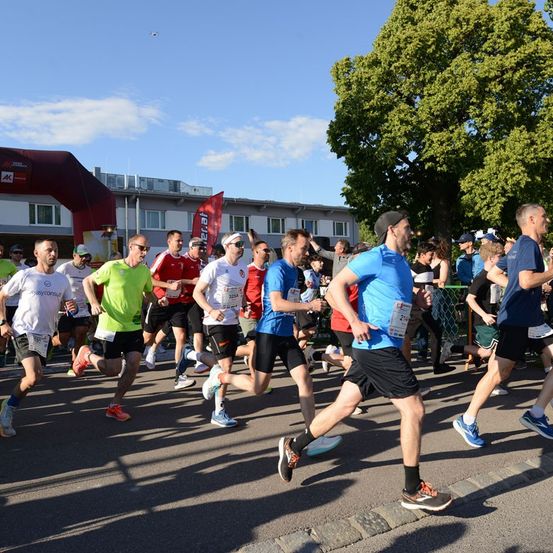 Eine Gruppe von Läufern in verschiedenen farbigen Shirts und Shorts nimmt an einem Marathon an einem sonnigen Tag teil.