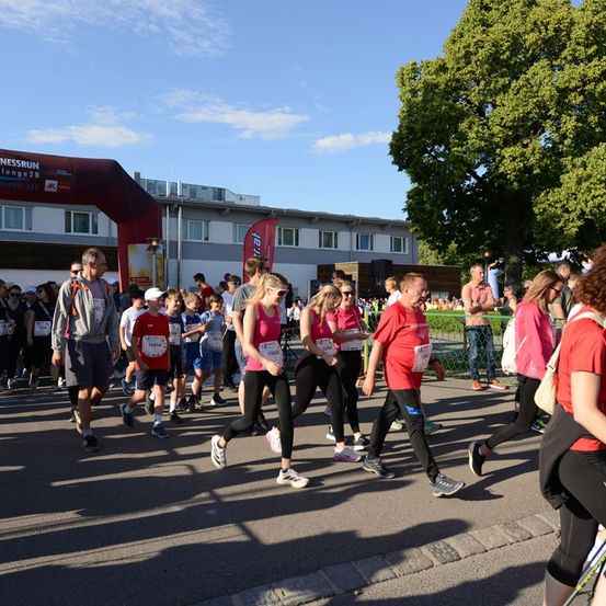 Eine Gruppe von Menschen nimmt an einem Marathon teil und läuft auf einer Straße mit einem roten Bogen und einem Gebäude im Hintergrund.
