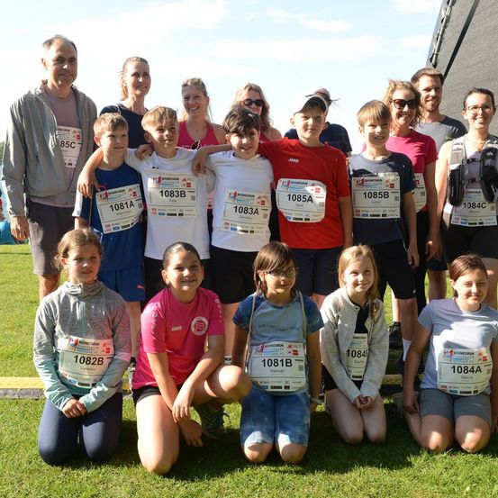 Eine Gruppe von Marathonteilnehmern, die nummerierte Startnummern tragen, posiert für ein Foto auf einem Rasenfeld.