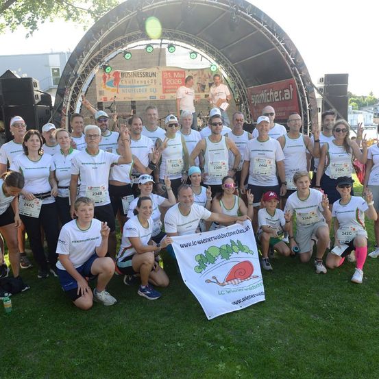 Eine Gruppe von Menschen in weißen Shirts mit Nummern posiert für ein Foto vor einer Bühne mit Banner und Lichtern.