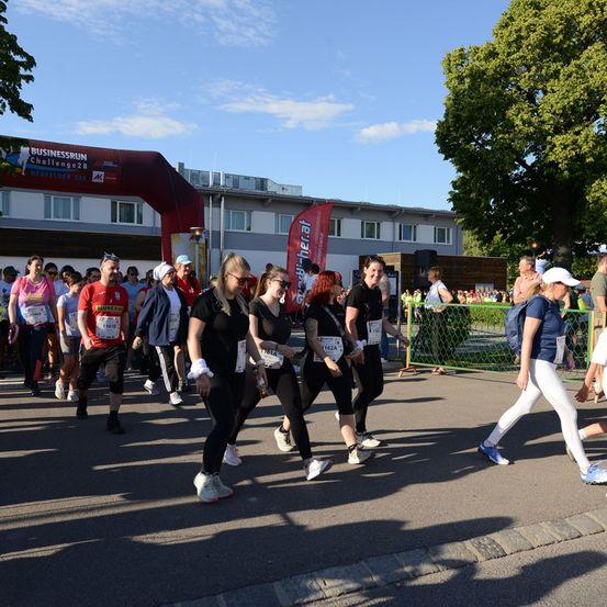 Teilnehmer eines Marathons, die nummerierte Startnummern tragen, laufen durch einen Zielbogen. Die Veranstaltung wird von Businessrun Challenge28 gesponsert.