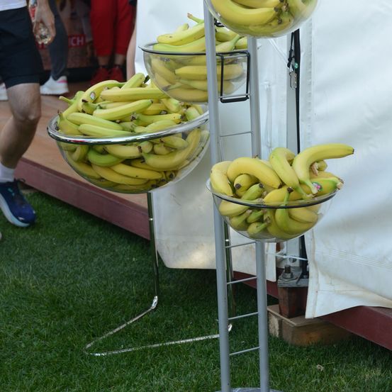 Eine Anzeige von Bananen in drei Glasschüsseln auf einem Metallständer, mit einer Person im Hintergrund.
