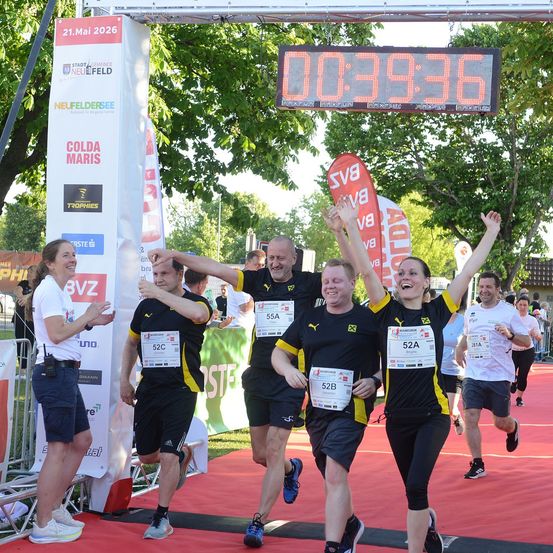 Eine Gruppe von Läufern beendet einen Wettkampf, wobei ein Läufer eine digitale Uhr mit der Zeit 00:39:36 hochhält. Sie tragen alle schwarze und gelbe Uniformen.