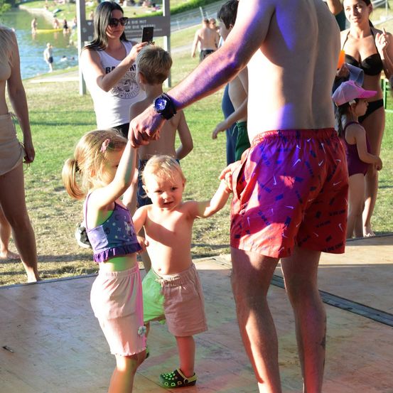 Ein Mann hält die Hände von zwei kleinen Kindern auf einer Bühne vor einer Menschenmenge am Strand.
