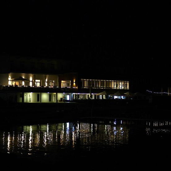 Ein Gebäude mit mehreren Fenstern und Lichtern, die sich nachts im Wasser spiegeln.