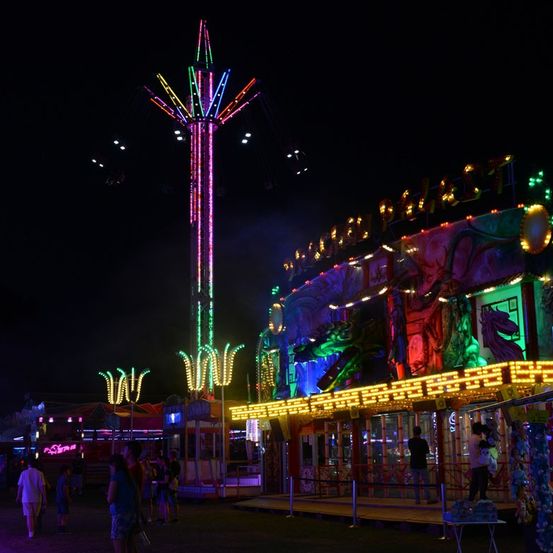 Ein leuchtendes Nachtfest mit einem bunten Riesenrad und beleuchteten drachenthematischen Attraktionen, das eine Menge Menschen anzieht.