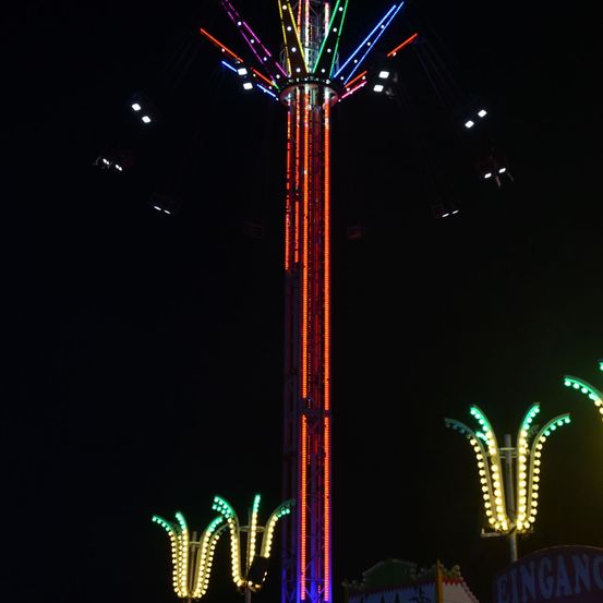 Ein hoher, bunter Vergnügungspark-Fahrt mit mehreren Armen, die sich nach außen erstrecken, nachts mit roten, blauen und grünen Lichtern beleuchtet.