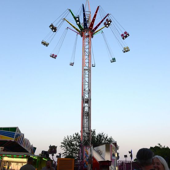 Ein großer, bunter Schaukel-Attraktion in einem Freiluft-Vergnügungspark mit Fahrgästen und anderen, die in der Nähe stehen.
