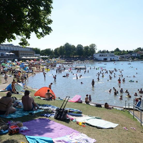 Eine überfüllte Strandszene mit vielen Menschen, die schwimmen, sich sonnen und das sonnige Wetter draußen genießen.