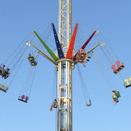 Ein bunter Schaukelsitz mit mehreren Sitzen, die von einem hohen Turm unter einem klaren blauen Himmel aufgehängt sind.