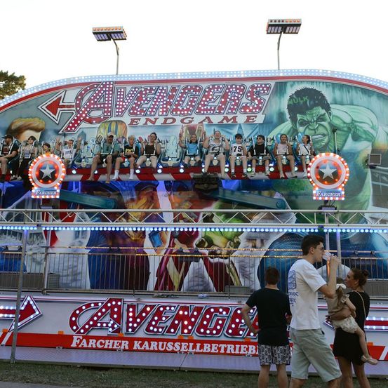 Achterbahn im Vergnügungspark mit Avengers Endgame-Thema, auf der Menschen sitzen und ein Mann ein Kind vor sich hält.