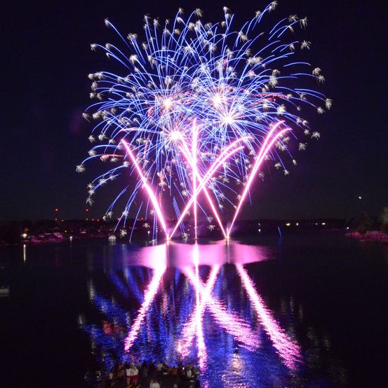 Ein leuchtendes Feuerwerk über einem See mit Reflexionen im Wasser bei Nacht.
