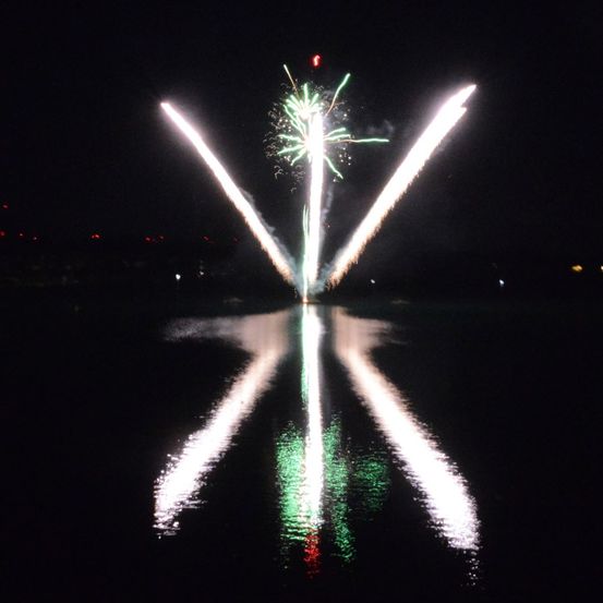 Ein Feuerwerksdisplay in der Nacht explodiert am Himmel, mit seiner Reflexion, die auf dem Wasser darunter schimmert.