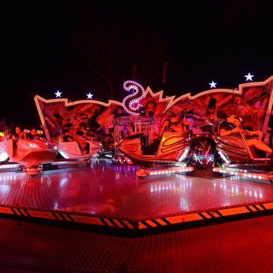 Ein Nachtattraktion im Vergnügungspark mit roten Lichtern und einer großen Nummer 2 oben, mit Menschen auf Booten.