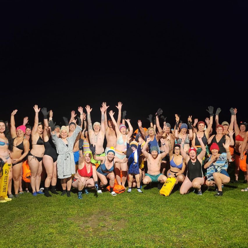 Eine Gruppe von Menschen, die in Badekleidung und Mützen gekleidet sind, steht auf einem Grasfeld und posiert möglicherweise für ein Gruppenfoto bei Nacht.