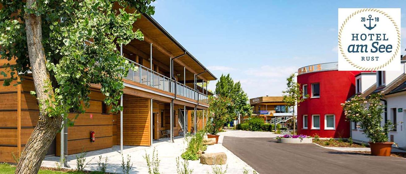 Ein modernes Holzhaus mit Glasgeländern auf dem Balkon, einem Feuerlöscher an der Wand und einem Baum davor.