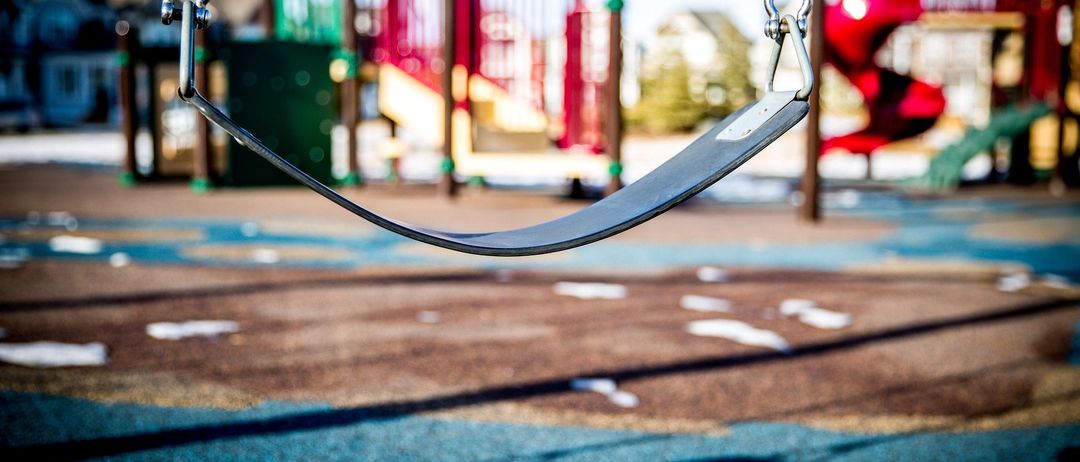 Ein Spielplatz mit einer Schaukel und einer Rutsche. Die Schaukel ist leer, und der Schatten der Schaukel fällt auf den Boden.