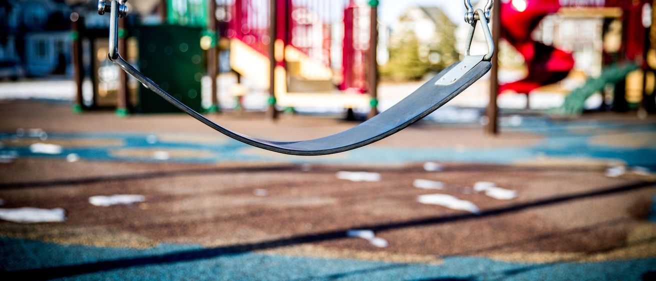 Ein Spielplatz mit einer Schaukel und einer Rutsche. Die Schaukel ist leer, und der Schatten der Schaukel fällt auf den Boden.