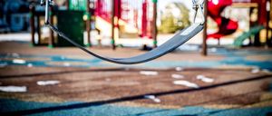 A playground with a swing set and a slide. The swing is empty, and the shadow of the swing falls on the ground.