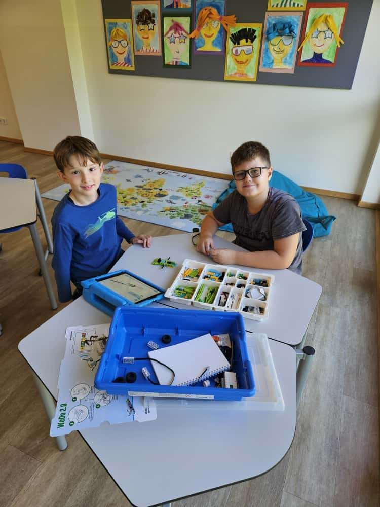 Zwei Jungen in einem Klassenzimmer mit einem Tisch voller Bausteine und einem Tablet. Ein Junge trägt eine Brille.