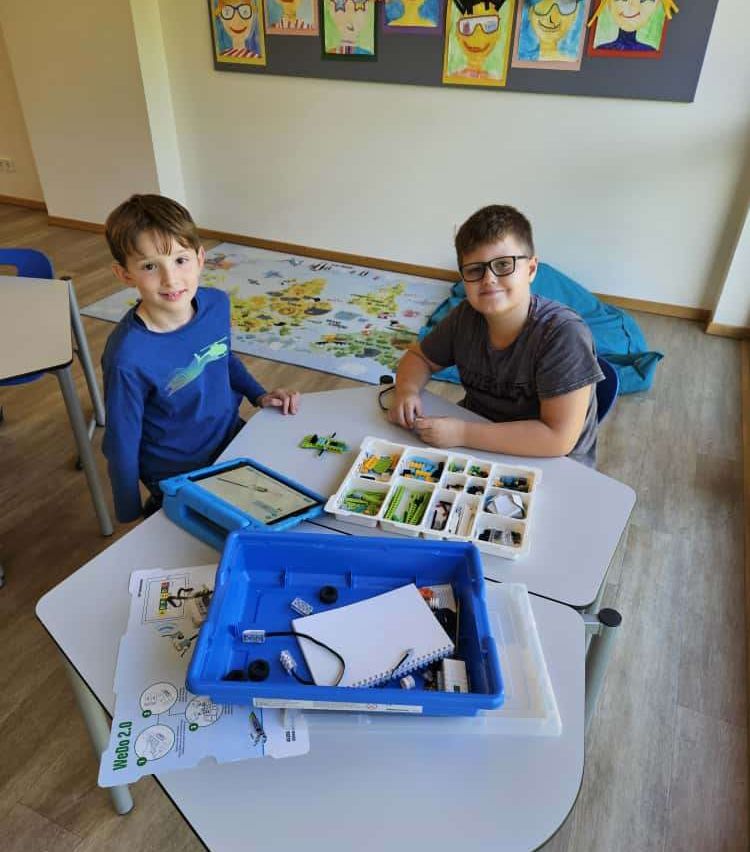 Zwei Jungen in einem Klassenzimmer mit einem Tisch voller Bausteine und einem Tablet. Ein Junge trägt eine Brille.