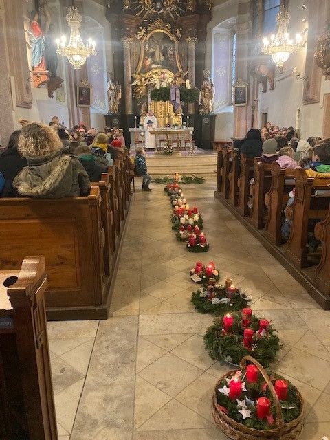 Ein Gottesdienst mit einem Priester am Altar, umgeben von Menschen und brennenden Kerzen auf dem Boden.
