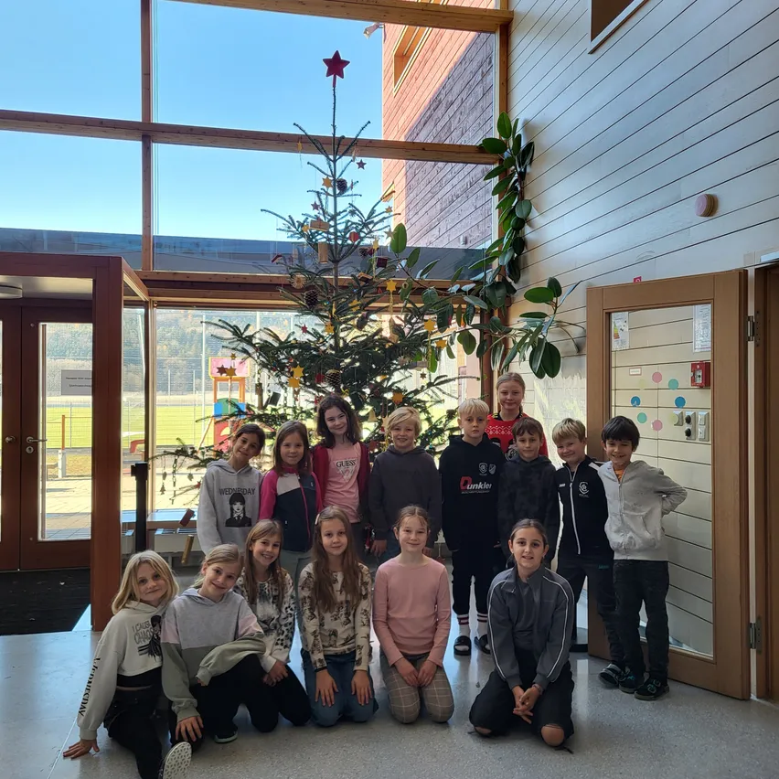 Eine Gruppe von Kindern und Jugendlichen posiert für ein Foto vor einem Weihnachtsbaum und dekorativen Elementen in einem Gebäudeflur.