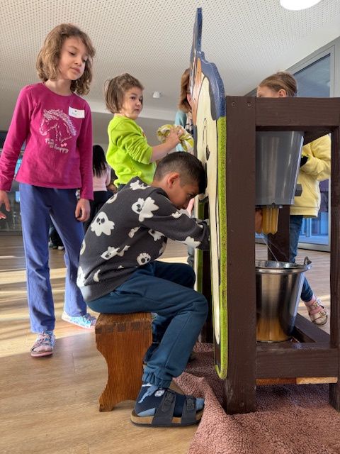 Ein Junge drückt einen Hebel an einer Holzmaschine, während andere stehen und ihn anschauen.