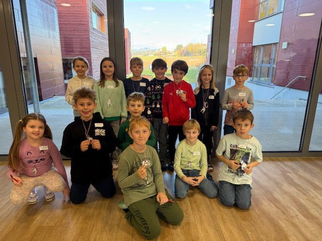 Eine Gruppe junger Kinder in Weihnachtspullovern posiert für ein Foto in einem Schulkorridor mit Holzböden.