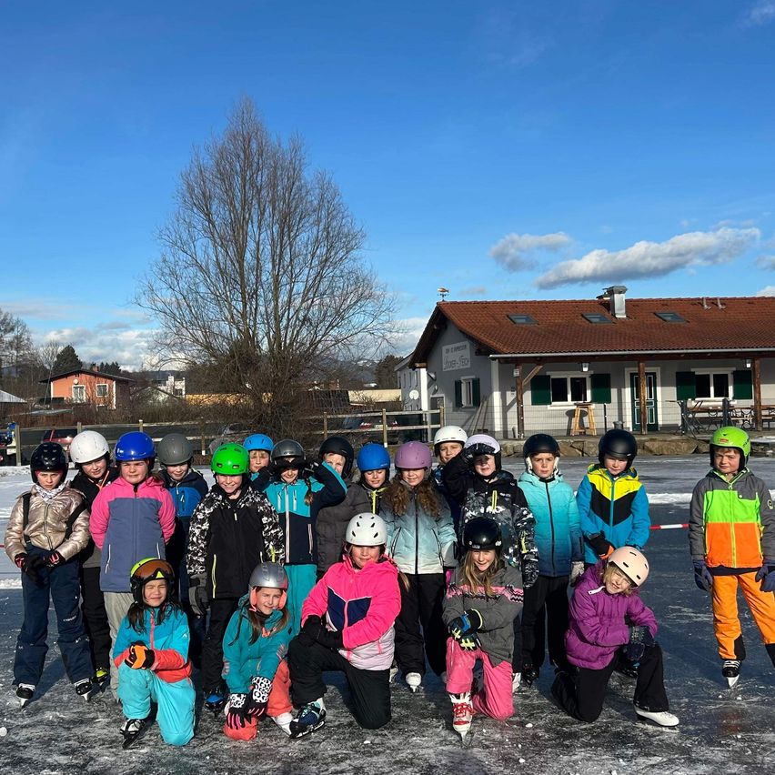 Eine Gruppe von Kindern in Winterkleidung posiert für ein Foto auf einer Eisbahn mit einem Haus im Hintergrund.