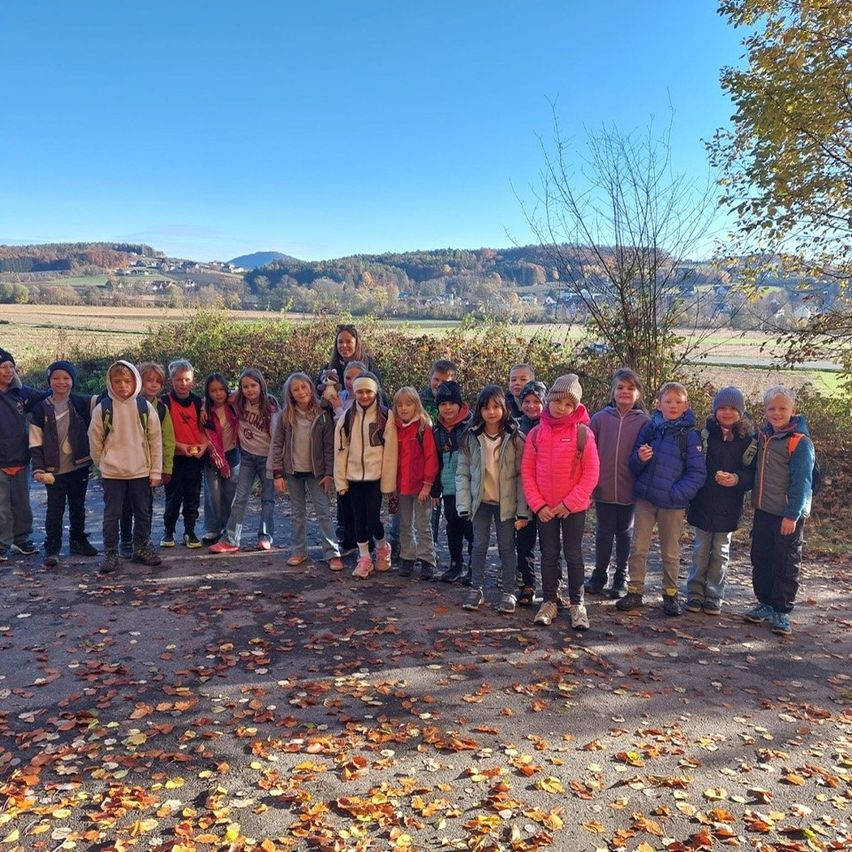 Eine Gruppe von Kindern posiert für ein Foto auf einem schotterweg mit gefallenen Blättern in einem ländlichen Gebiet.