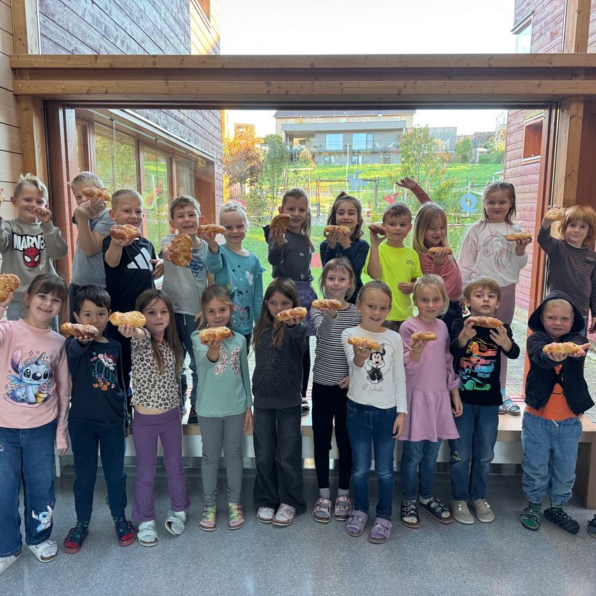 Eine Gruppe von Kindern posiert für ein Foto und hält Brot in den Händen. Sie lächeln und stehen vor einem Gebäude.