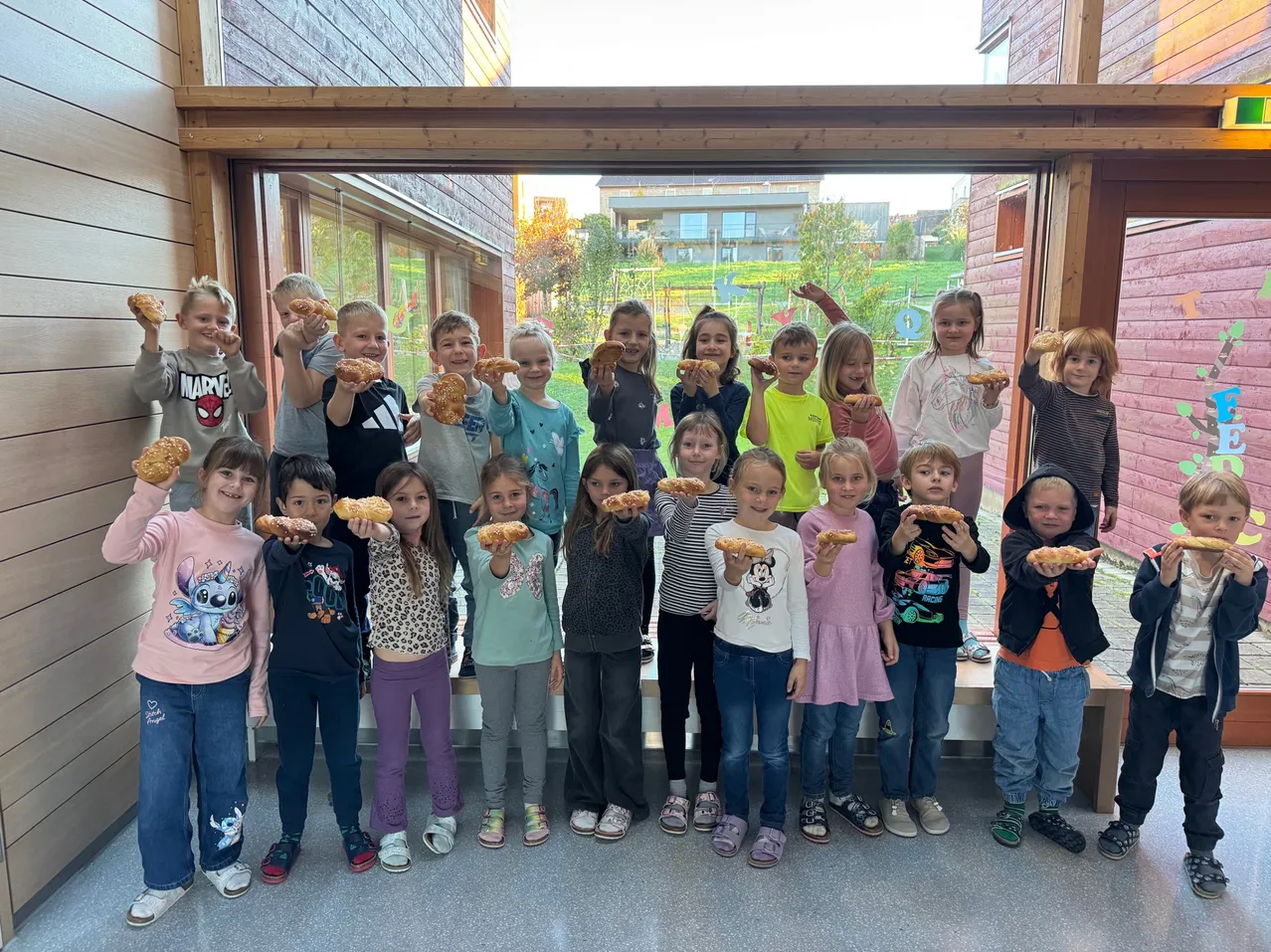 Eine Gruppe von Kindern posiert für ein Foto und hält Brot in den Händen. Sie lächeln und stehen vor einem Gebäude.