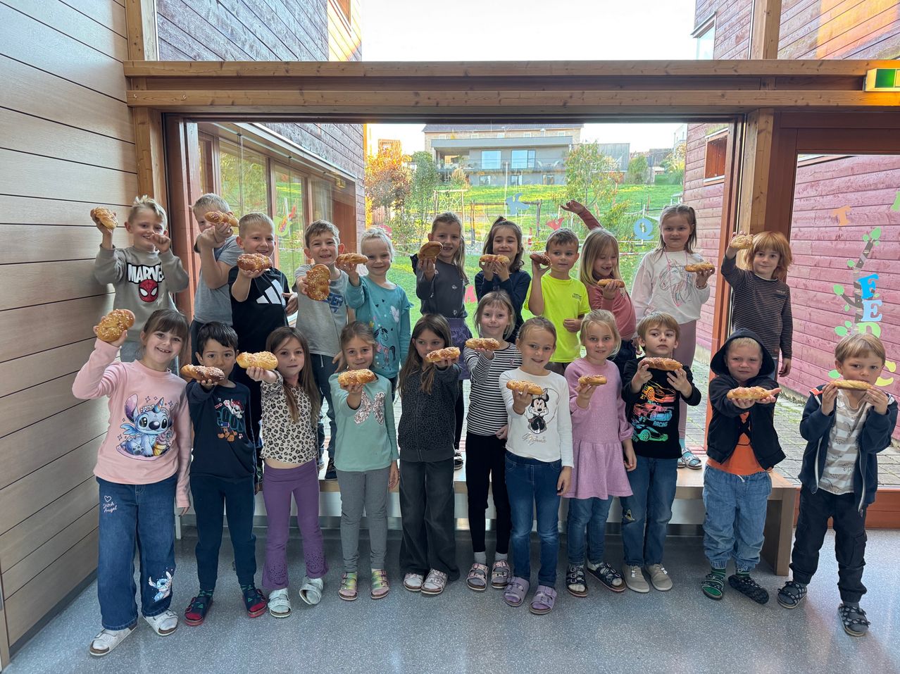 Eine Gruppe von Kindern posiert für ein Foto und hält Brot in den Händen. Sie lächeln und stehen vor einem Gebäude.